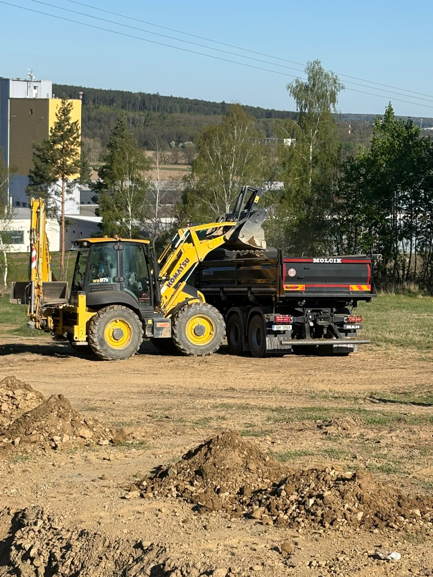 Traktorbagr Komatsu WB 97 nakládá sklápěč MAN na stavbě